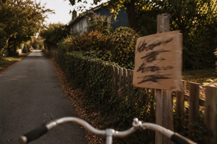 View from a bicycle passing a blank event poster on a suburban path